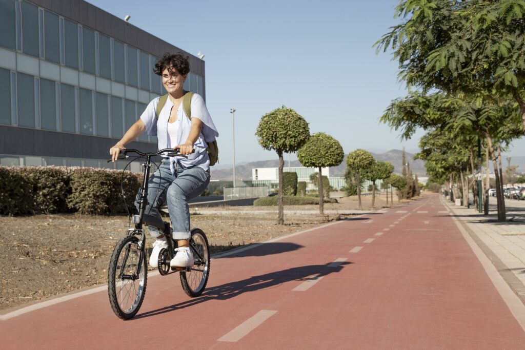 mulher de mochila andando sorridente de bicicleta em uma ciclovia arborizada
